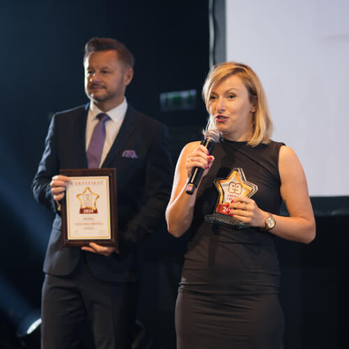Przedstawicielka DPD Polska odbiera nagrodę Gwiazda Jakości Obsługi 2024 podczas uroczystej gali. Na zdjęciu kobieta trzymająca statuetkę i mikrofon, obok mężczyzna z certyfikatem.